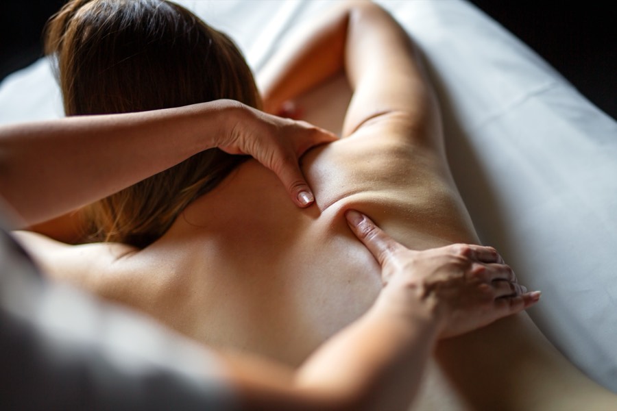 A therapist's hands pressing into the muscles of a client's upper back and shoulder.